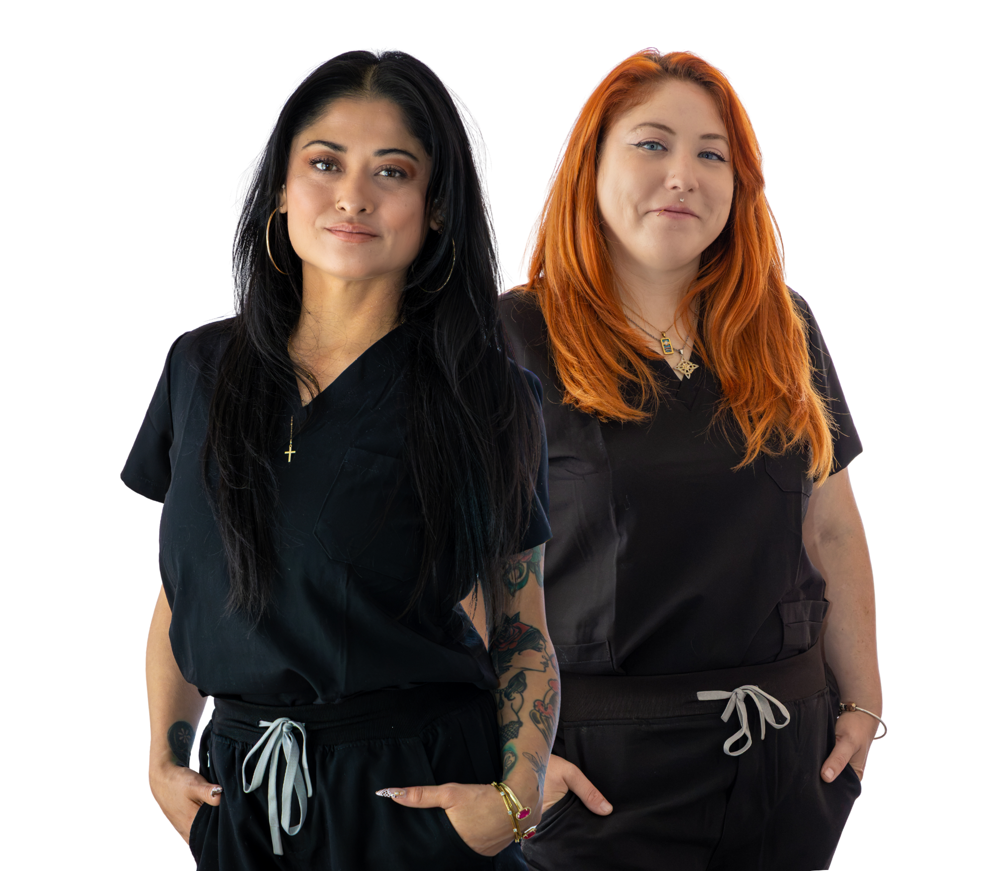 Two women standing side by side, one with black hair and the other with red hair, both wearing black medical scrubs with jewelry.