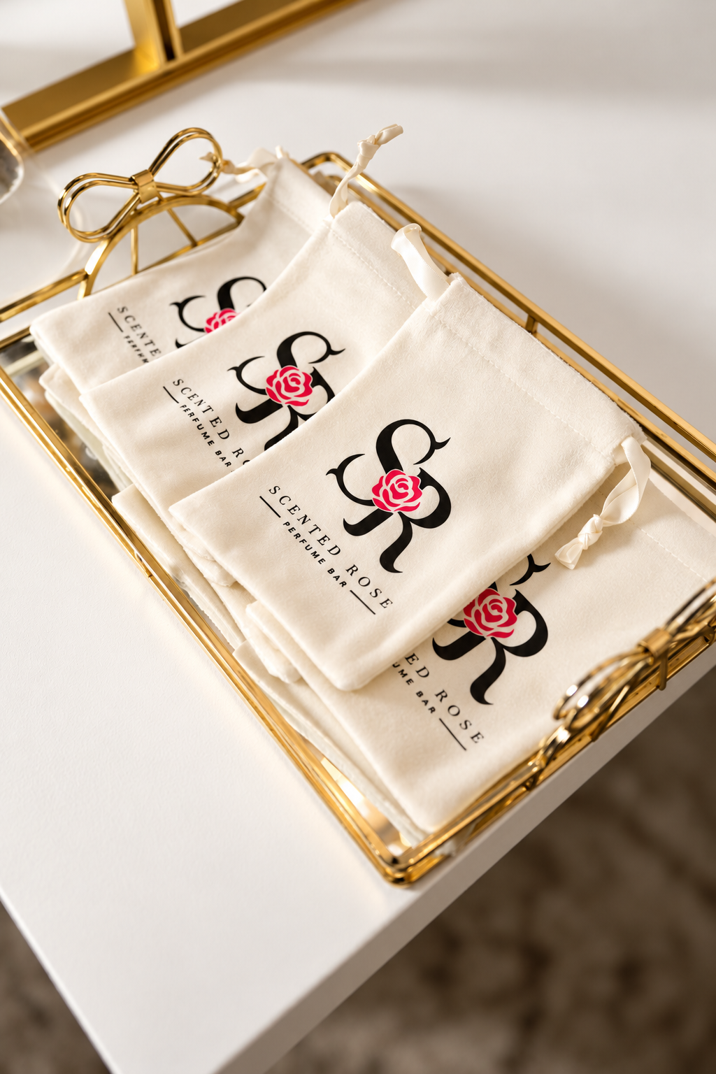 Cream drawstring bags labeled “Scented Rose Perfume Bar” arranged in a gold tray.