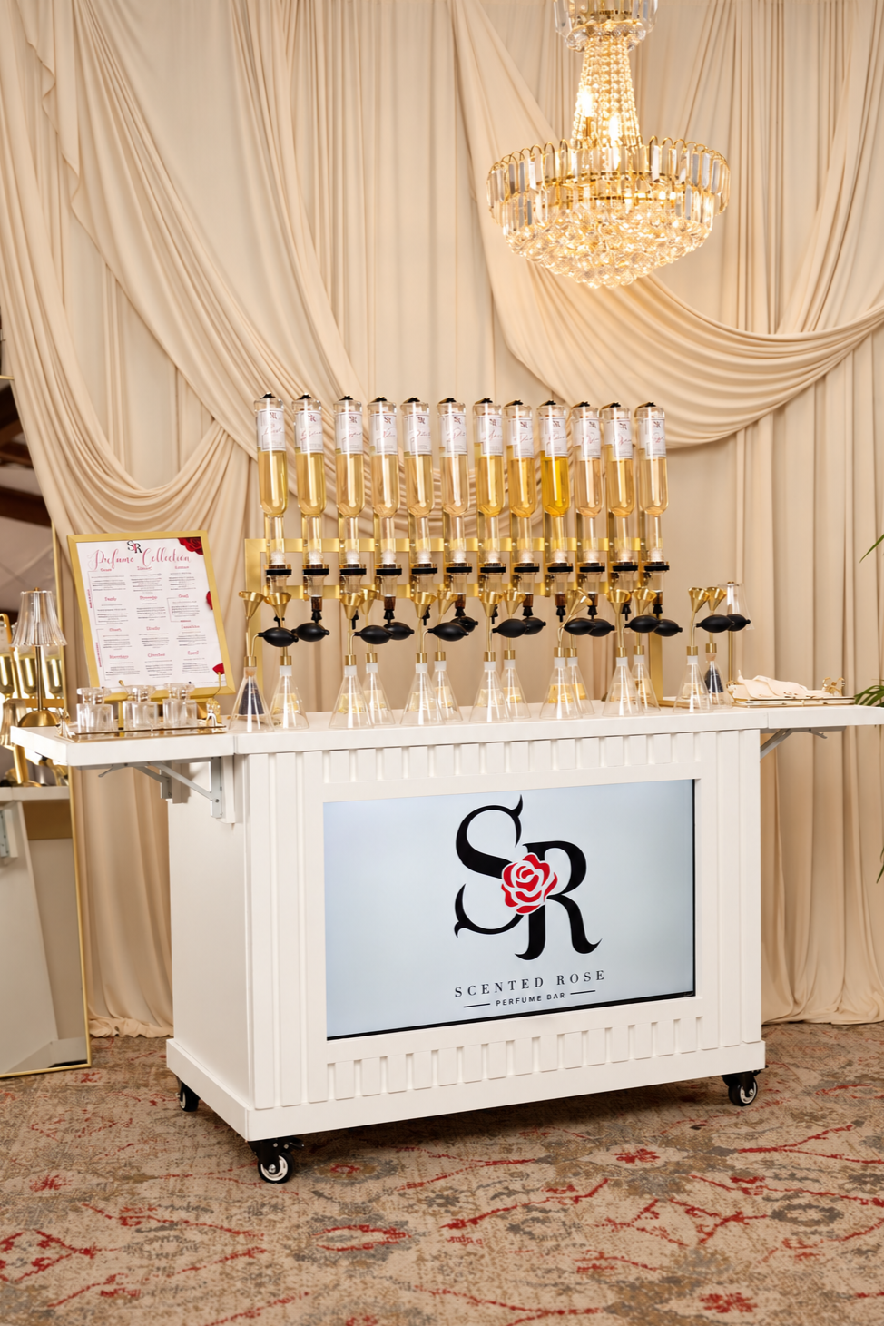 Scen­t­ed Rose perfume bar cart with fragrance bottles, display menu, and crystal chandelier