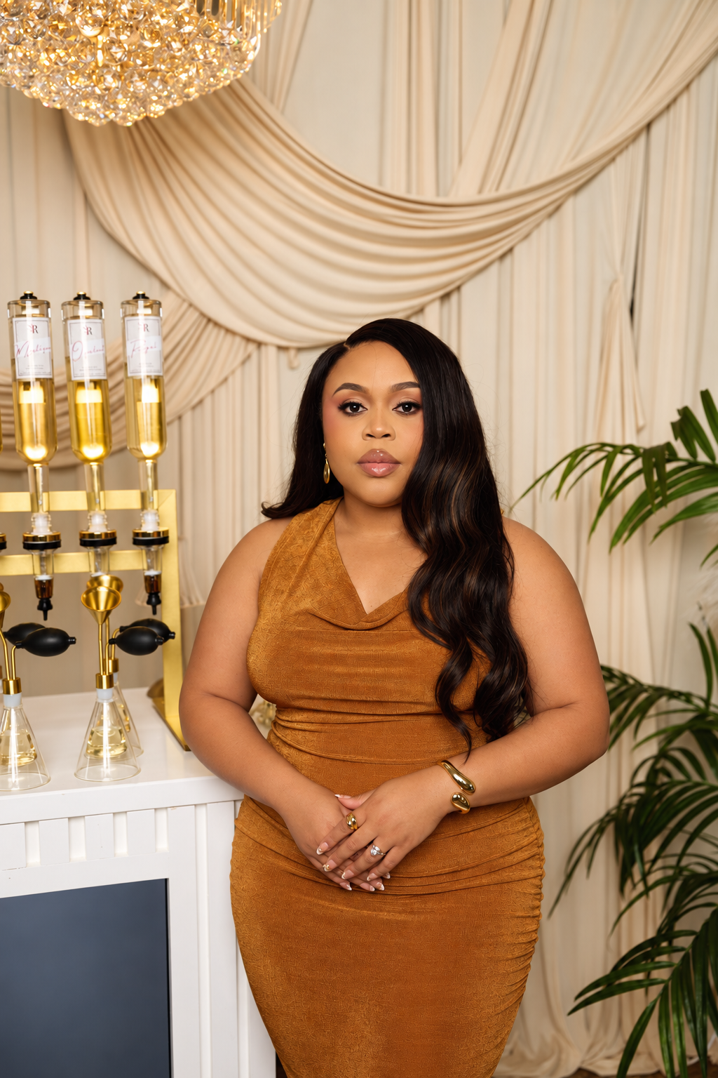 Woman in a rust-colored dress posing beside champagne bottles in an elegant draped room
