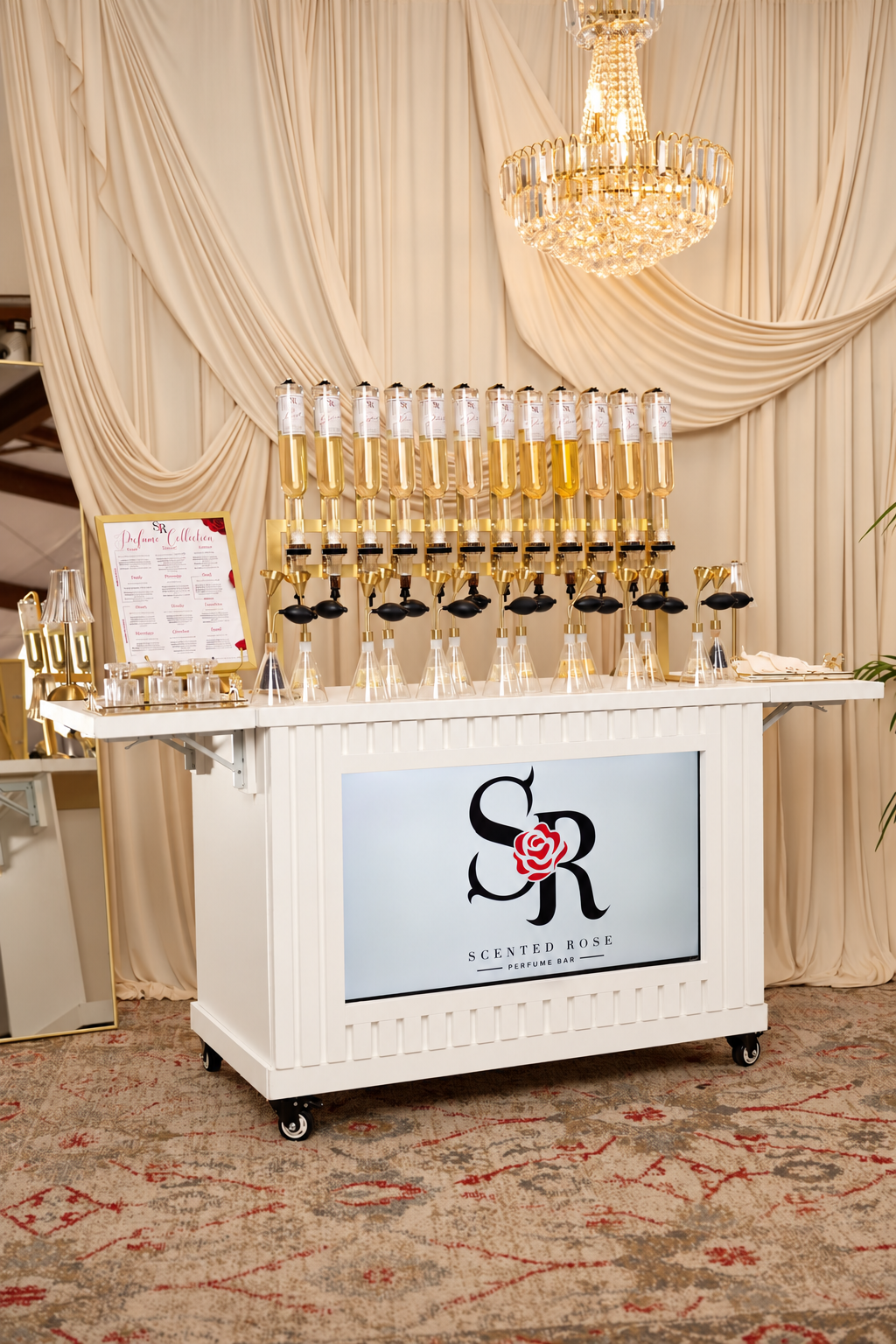 ScStented Rose perfume bar cart with perfume bottles, tasting tubes, chandelier, and draped cream backdrop