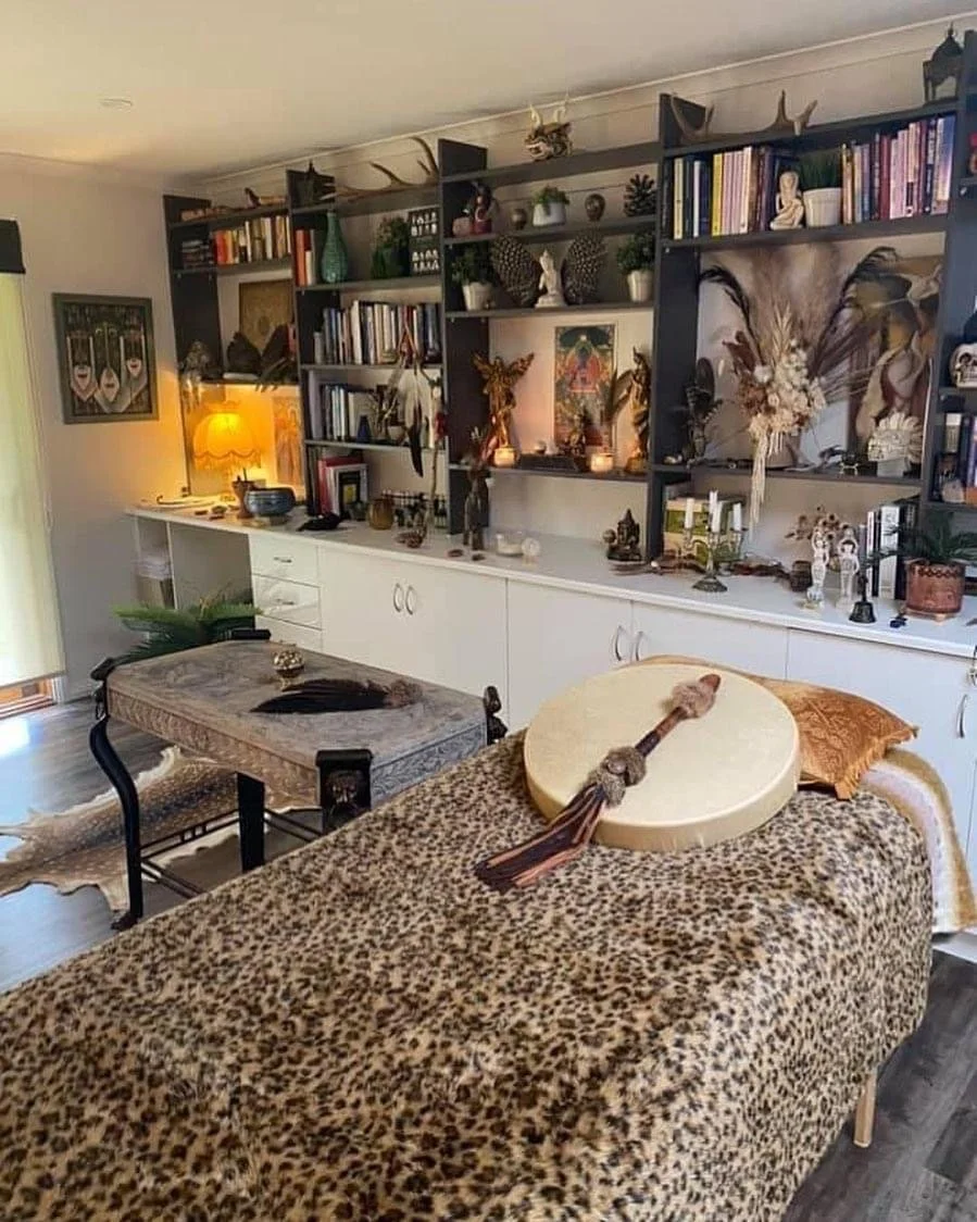 Living room with a bookshelf decorated with plants, books, and art, a leopard print cover on a table, a drum with a mallet on it, and various decorative items.