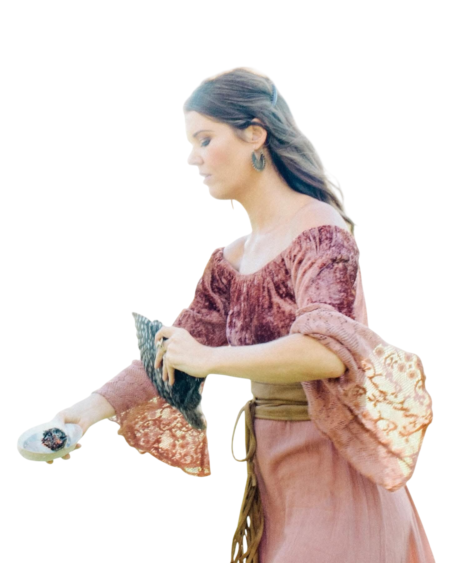 A woman with dark hair styled back, wearing jewelry and an elegant, vintage-style dress with lace and embroidery, sitting and holding a small dog in her lap while looking at her phone.