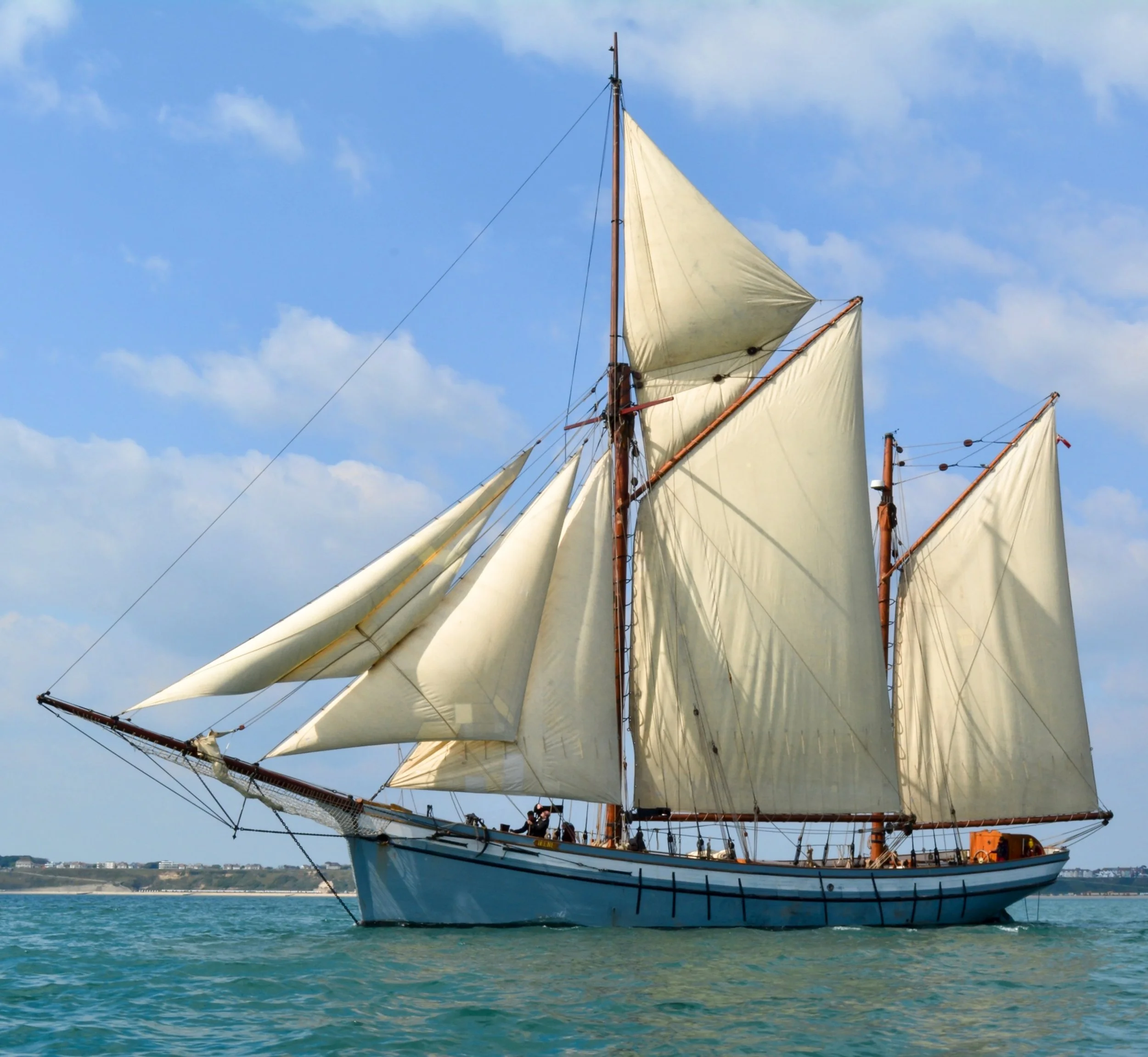 A traditional sailing ship with multiple cream-colored sails on a bright, partly cloudy day.