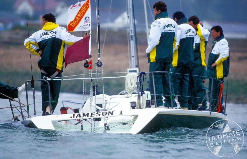 A group of six sailors on a sailboat labeled 'JAMESON 1', with some wearing matching team jackets, on a body of water during a sailing event.