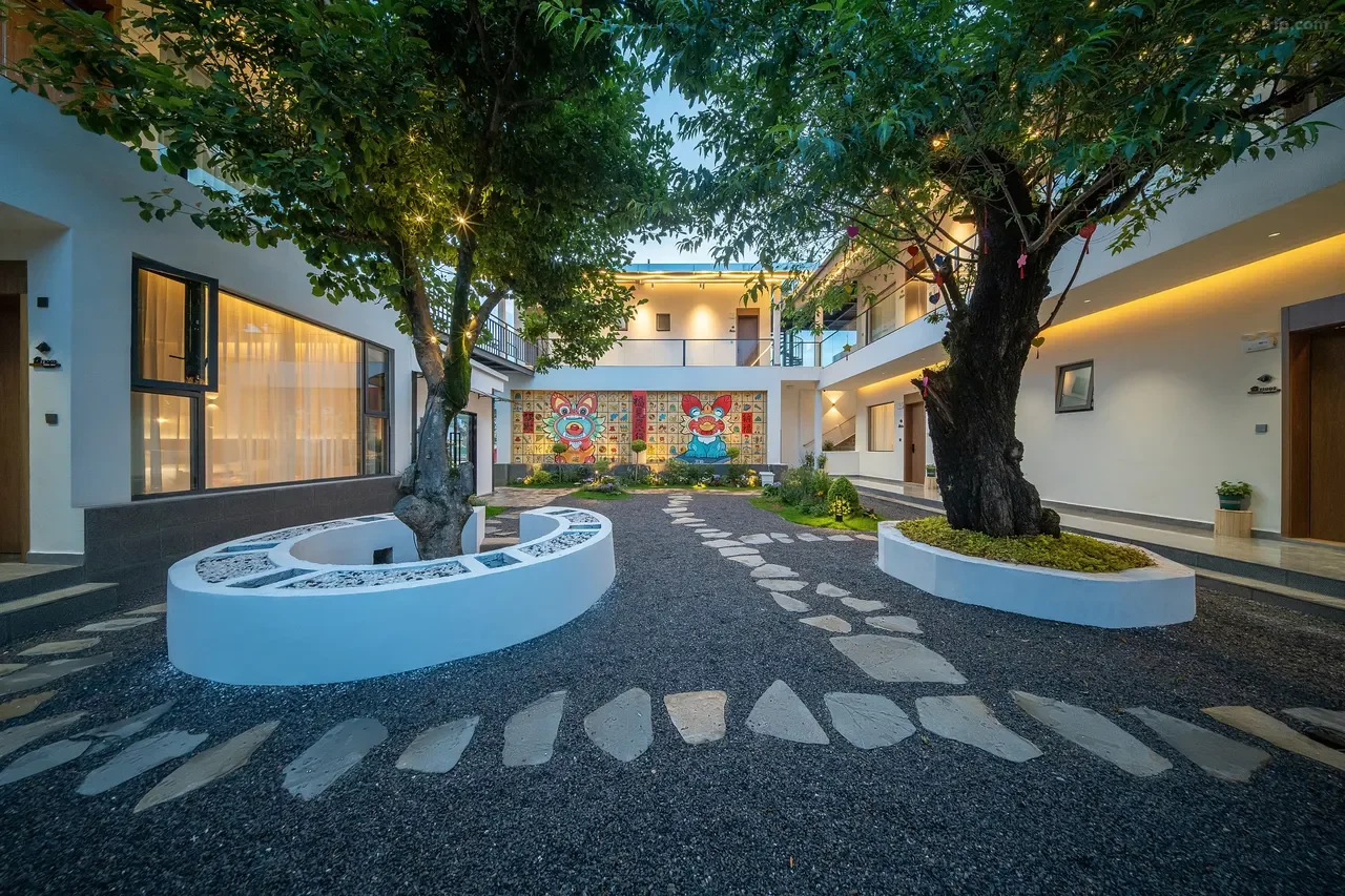 Courtyard of a modern building with two large trees, a stone pathway, and colorful artwork of animals on the wall in the background.