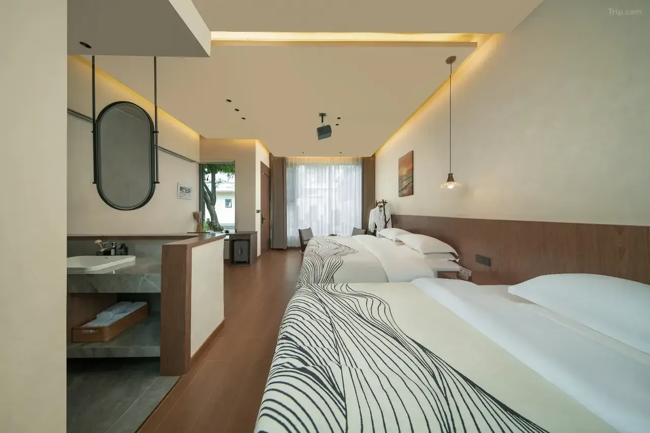 Modern hotel room with two beds, a sitting area near large window, and minimalistic decor.