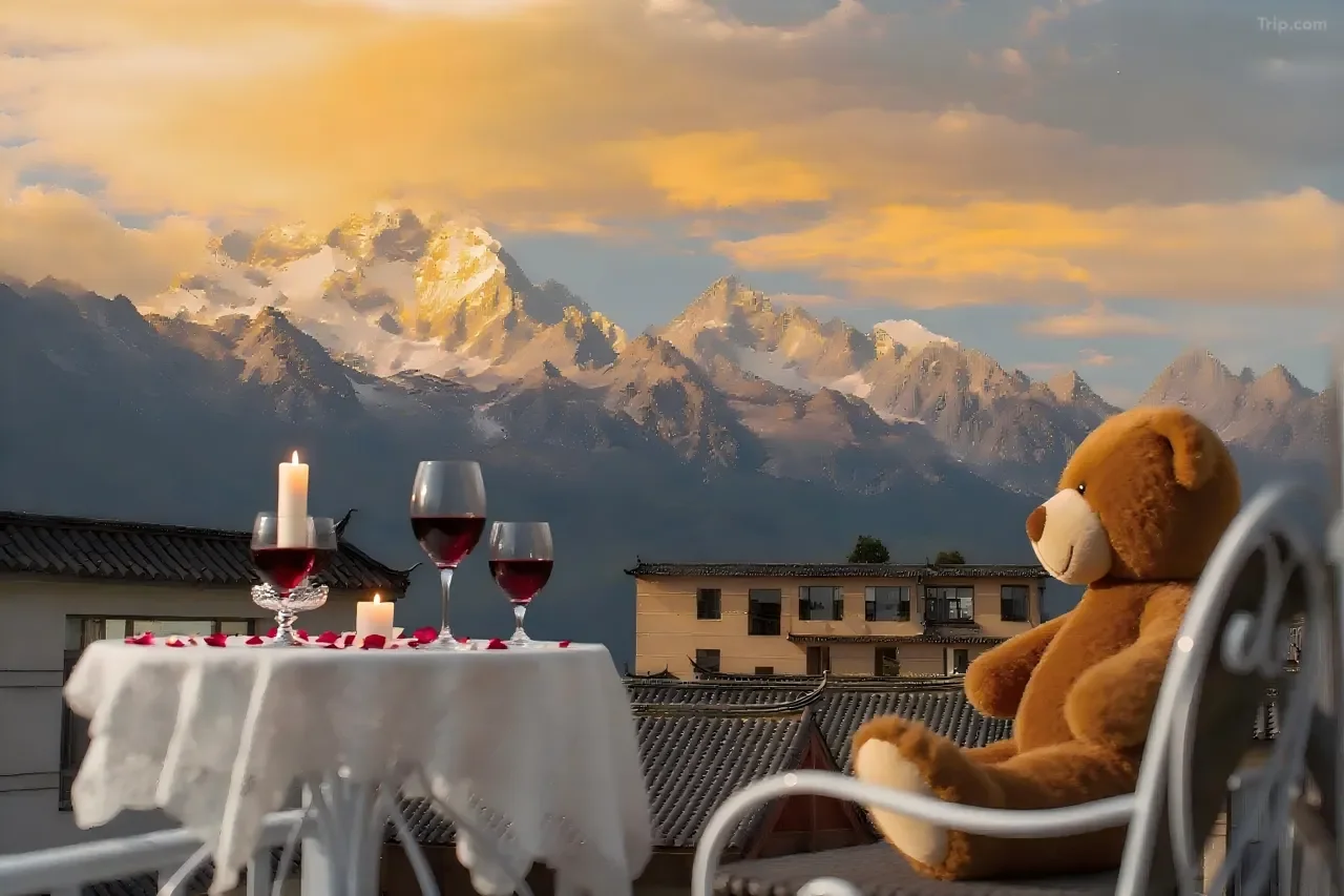 Teddy bear sitting on a balcony with a wine glass, candles, and rose petals, overlooking a mountain range during sunset.