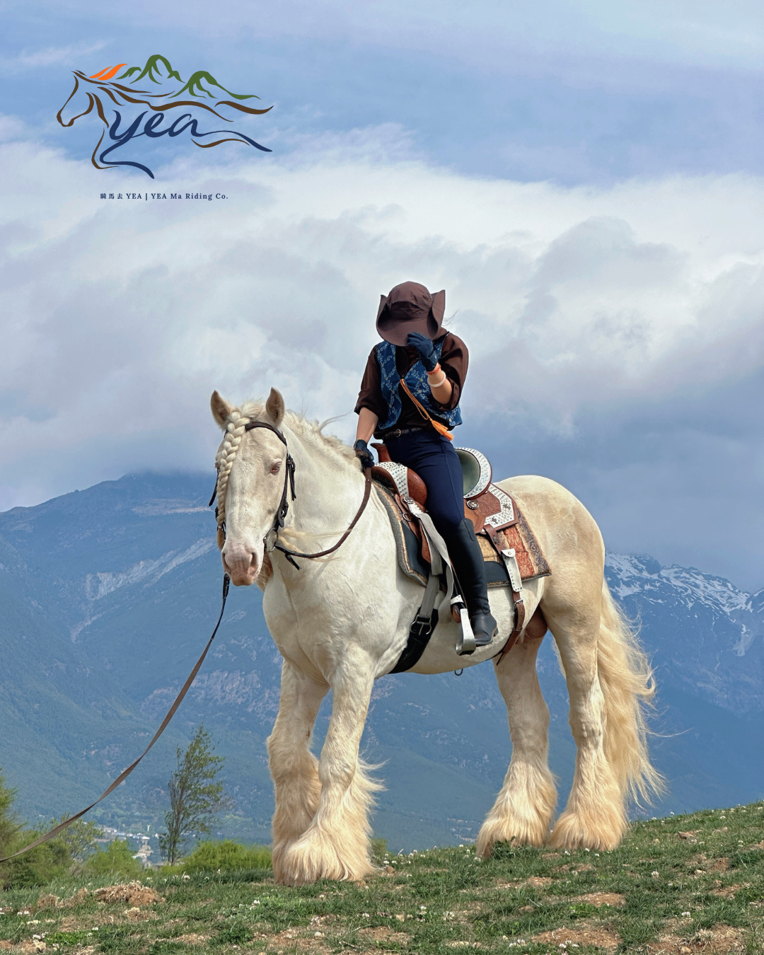 A person wearing a hat and riding a white horse in a mountainous landscape with cloudy sky.