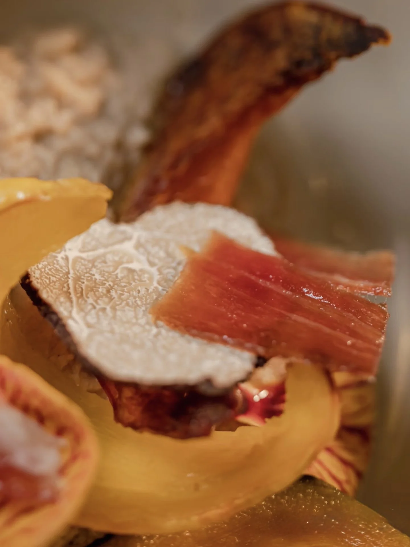 Close-up of crispy bacon slices placed on roasted vegetables, including cauliflower and potatoes.