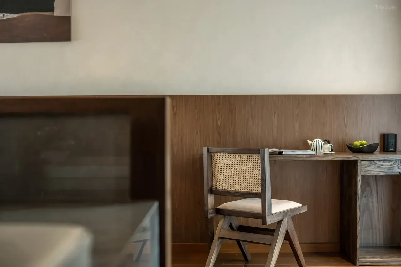 A wooden chair with a woven backrest and cushioned seat placed in front of a simple wooden desk or counter, with teapots, a cup, and a small bowl of limes on the surface.
