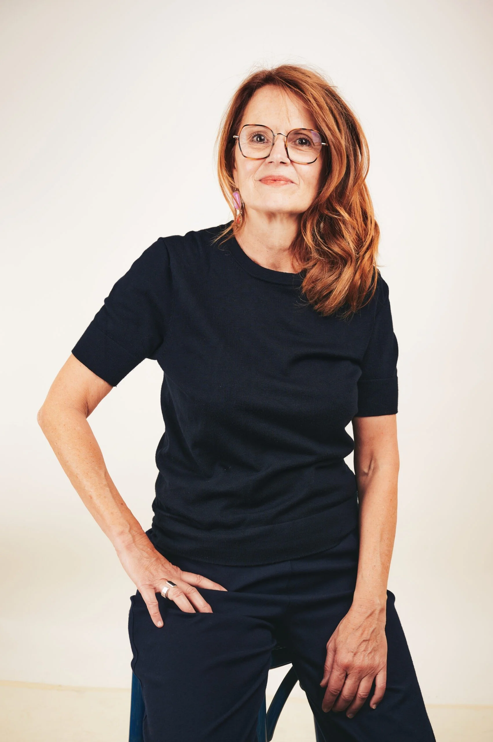 Femme avec lunettes, cheveux roux, portant un t-shirt noir, assise sur une chaise, photo en studio