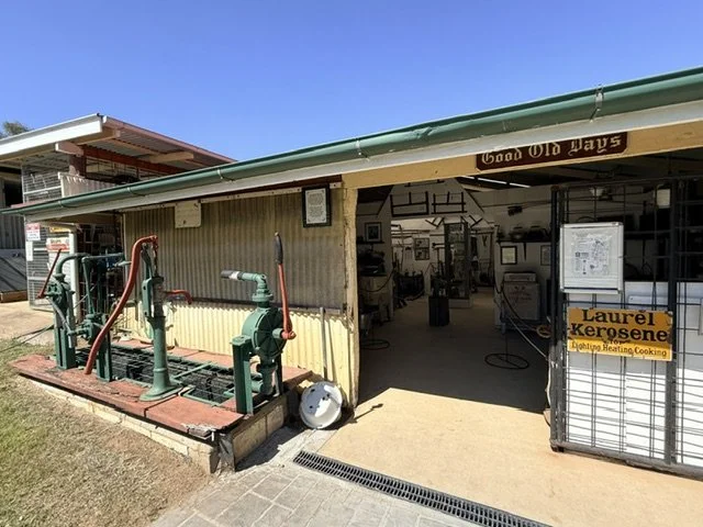 View of an outdoor firehouse station with fire hose equipment on the left and an open indoor area displaying firefighting gear and equipment. Sign on the right says "Laurel's Koresene" and mentions lighting, heating, and cooking.