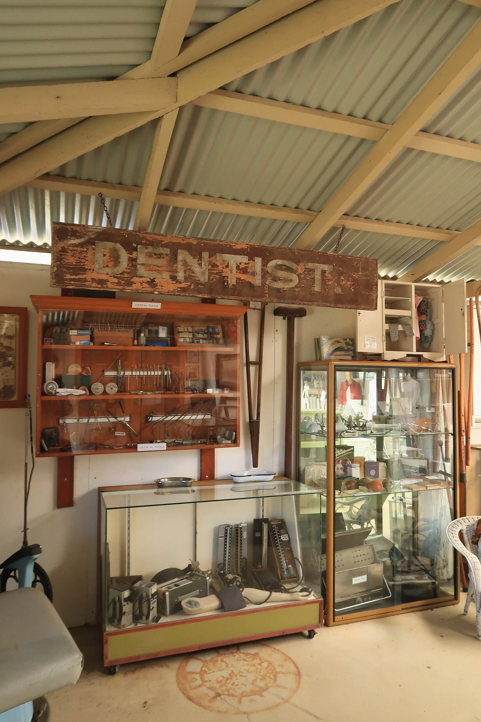 Vintage display of dental and medical tools in a glass-front cabinet at an antique shop with a large wooden 'DENTIST' sign hanging above.