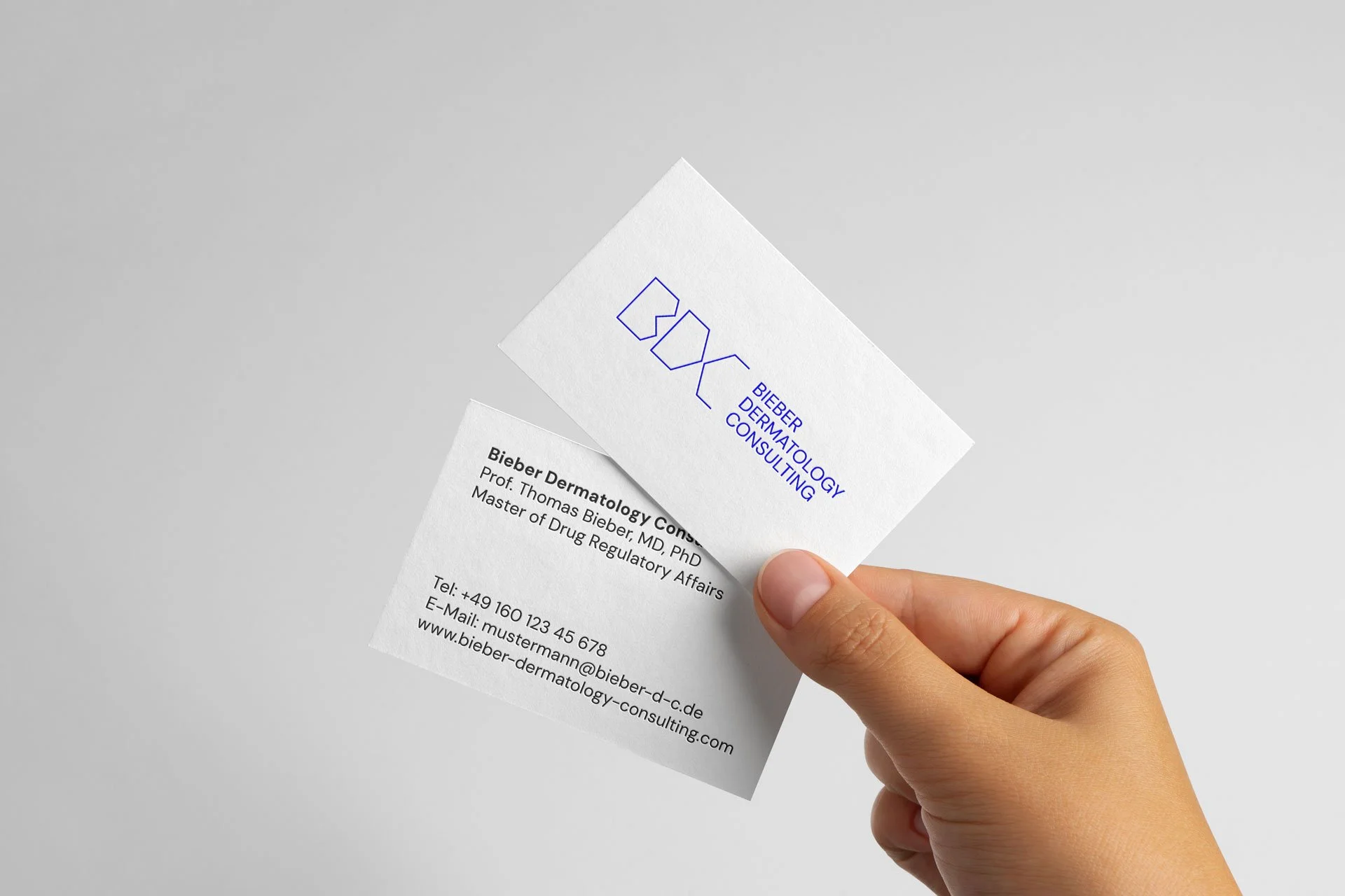 Nahaufnahme einer Hand, die Visitenkarten für die Biebert Dermatology Consulting hält, mit einer grauen neutralen Hintergrund.