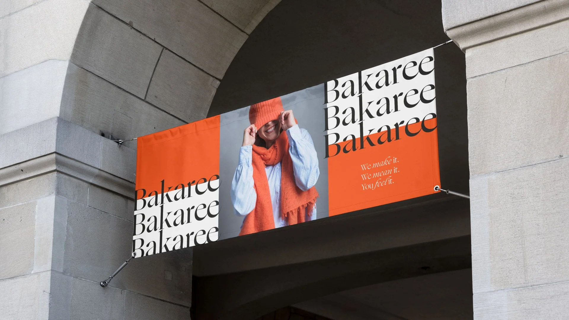 Werbung für die Marke Bakaree, mit einem lachenden Menschen, der eine orange Mütze und ein passendes Tuch trägt, auf einer orangefarbenen und weißen Hintergrundwand an einem Gebäude.