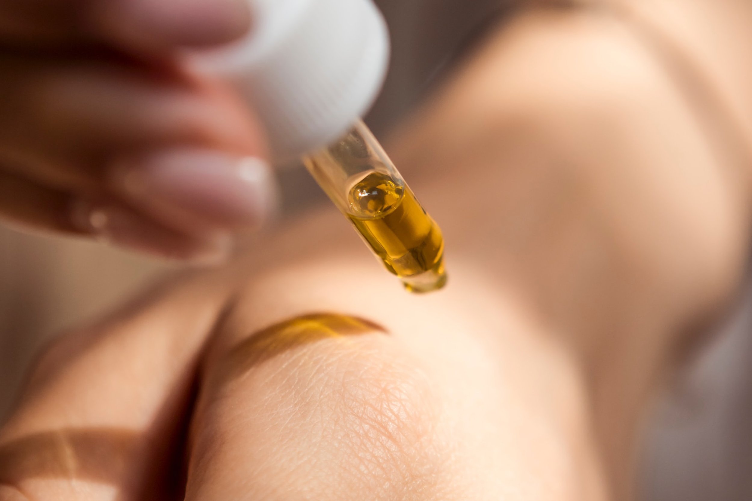 Nahaufnahme einer Pipette, die eine gelbe Flüssigkeit auf die Haut tropft.