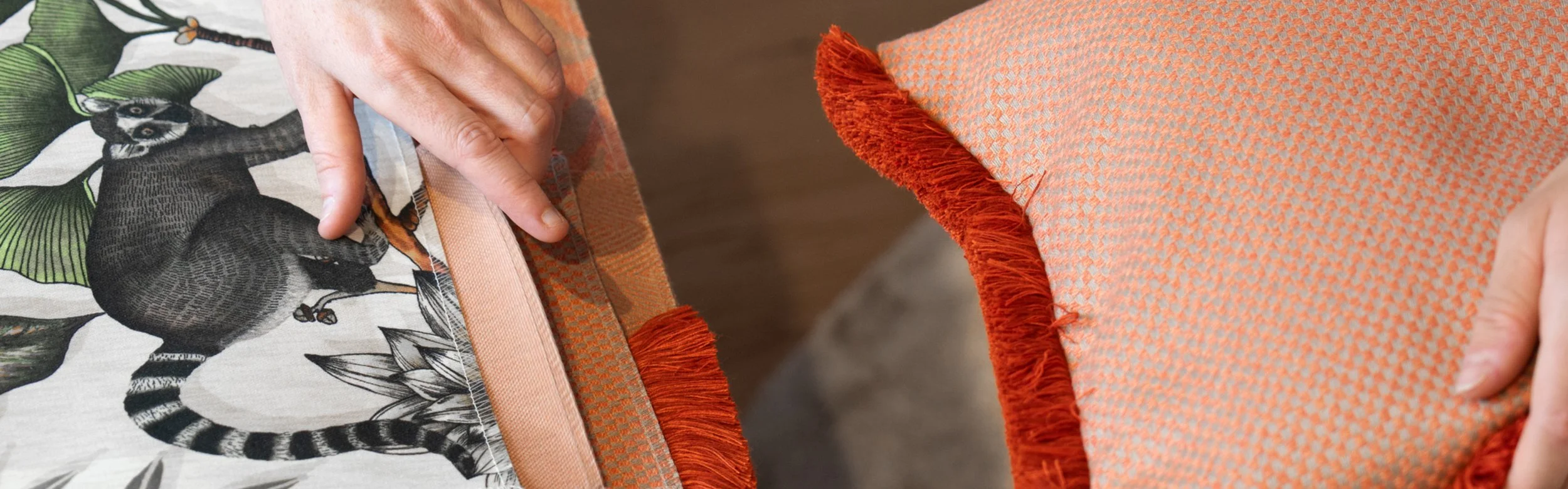 Person hält zwei Stoffe mit orangem Fransenrand, einer mit Tiermuster, der andere mit geometrischem Muster.