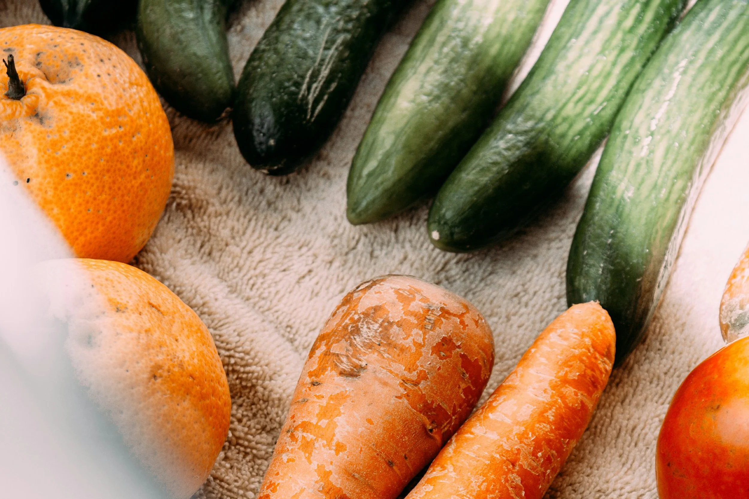 Verschiedene frische Zucchini, Süßkartoffeln und Orangen liegen auf einer Stoffoberfläche.