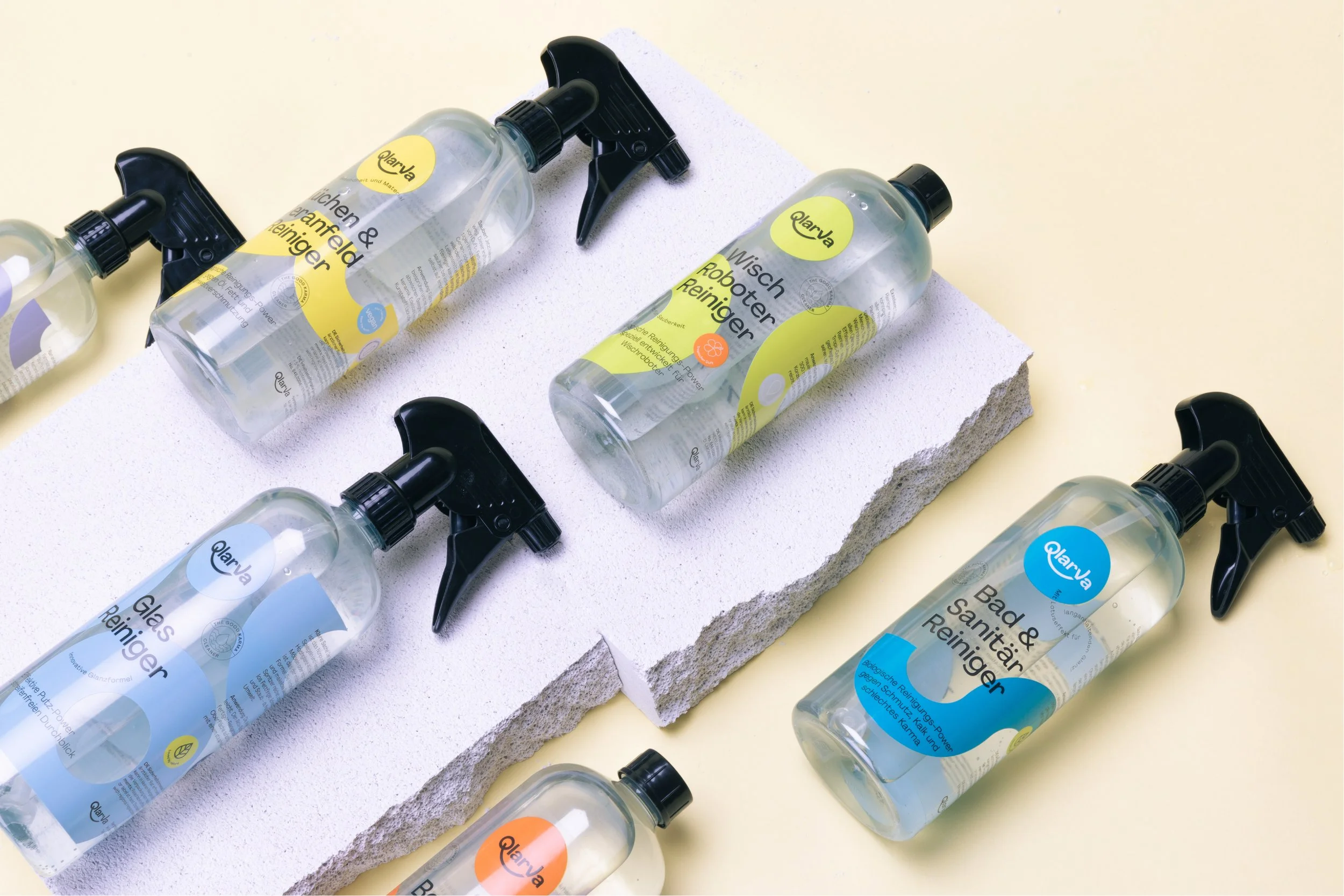 Mehrere Sprayflaschen mit Reinigungsprodukten stehen auf einer weißen Oberfläche. Die Flaschen haben schwarze Sprühköpfe und gelbe oder blaue Etiketten mit deutschen Texten.