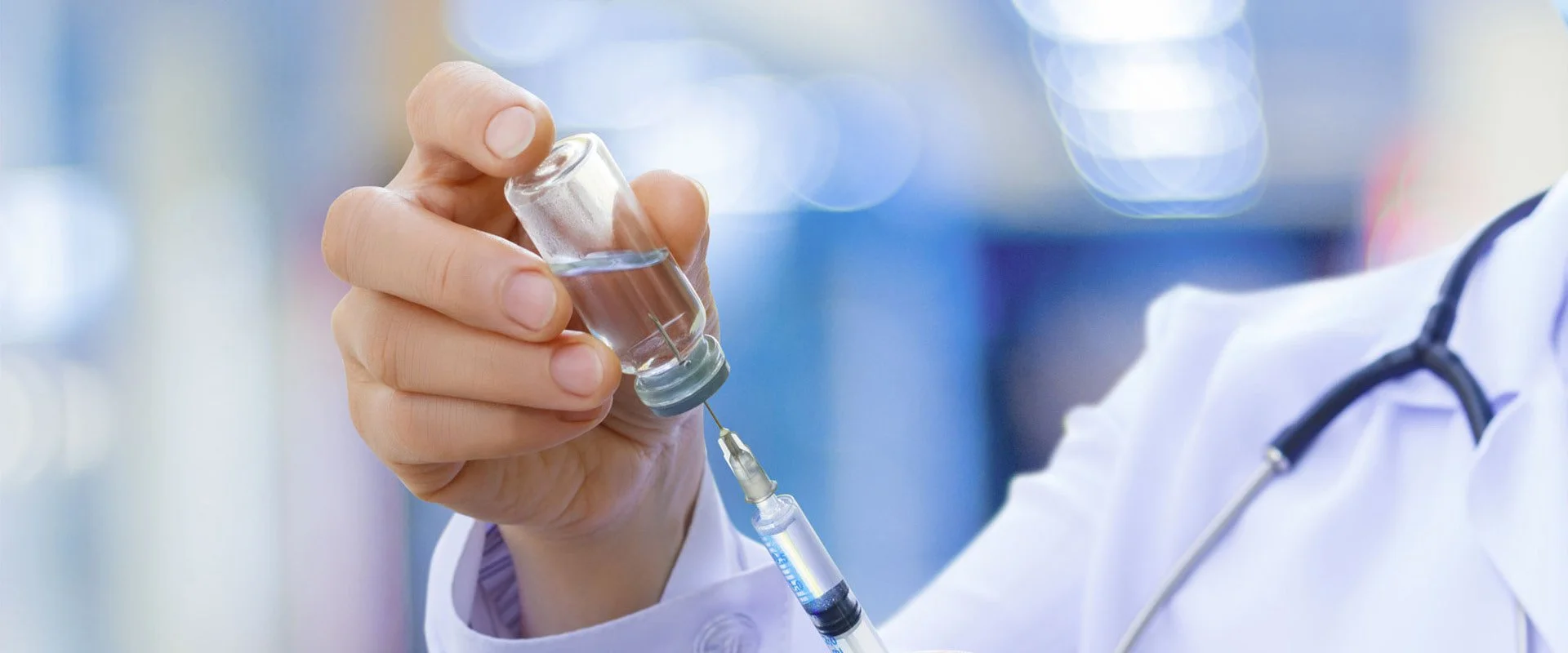 Arzt oder Wissenschaftler zieht eine Flüssigkeit mit einer Spritze aus einer kleinen Ampulle in einem medizinischen Umfeld.