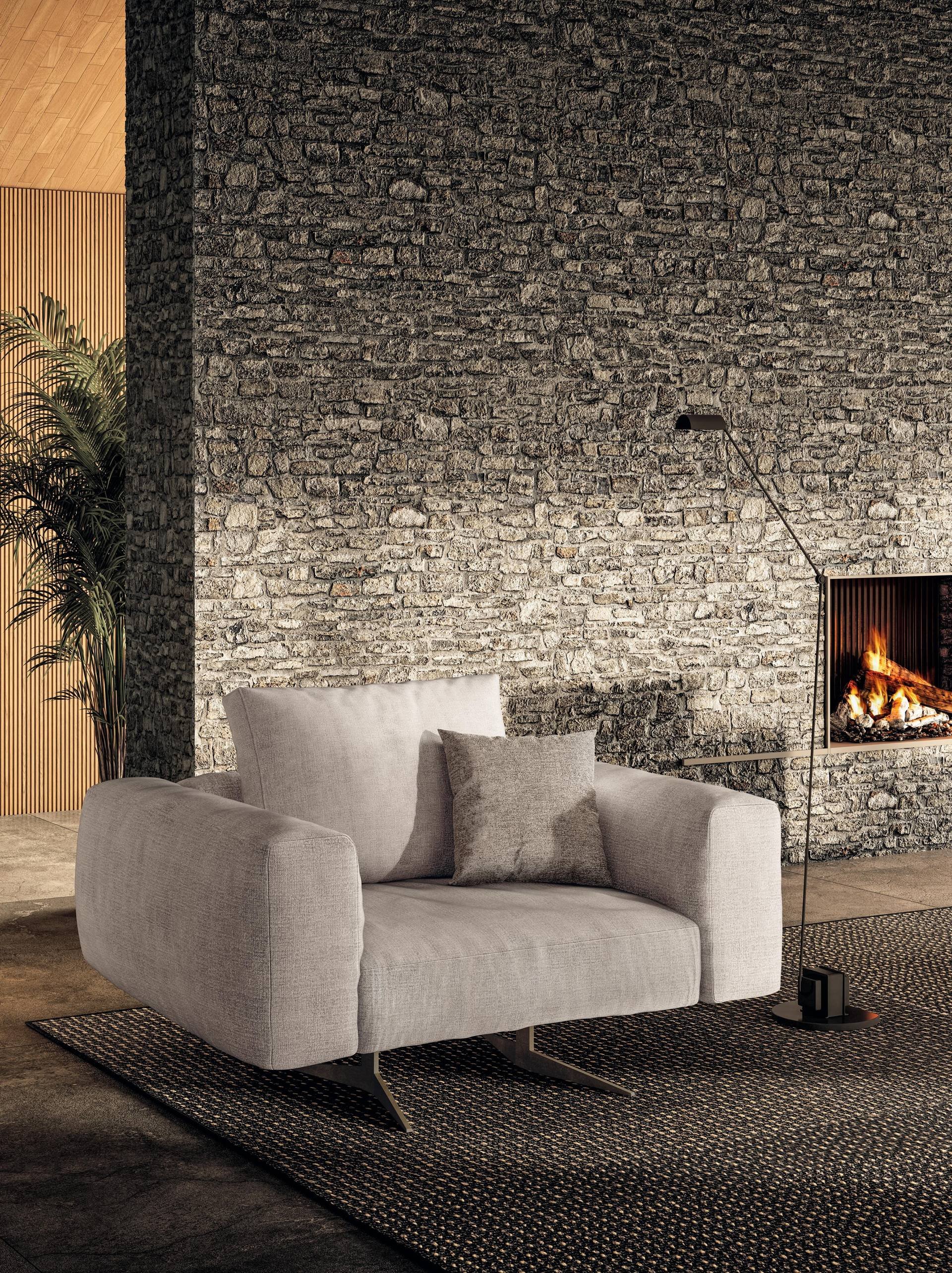 Modern living room with a concrete gray sofa, a gray accent pillow, a textured black area rug, metal chair sled base, a black floor lamp, a stone brick wall with a fireplace, and some green plants.