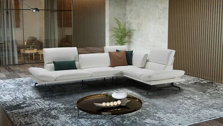 Modern living room with a white sectional sofa, decorative pillows, a round black coffee table with a white sculpture, and a textured gray rug.