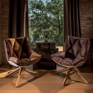 Two plush modern armchairs facing each other with a window showing trees outside in the background.