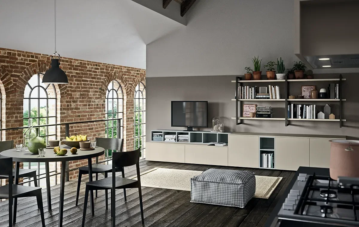 Modern living room with exposed brick wall, arched windows, and a dining table with black chairs, a TV on a low white console, wall-mounted shelves with plants and books, and a checkered ottoman.