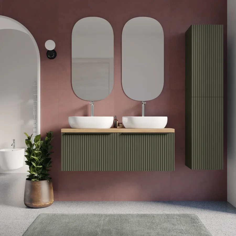 A modern bathroom with a pink wall, two oval mirrors above two sinks, a green cabinet and a potted plant, with a rug on the floor.