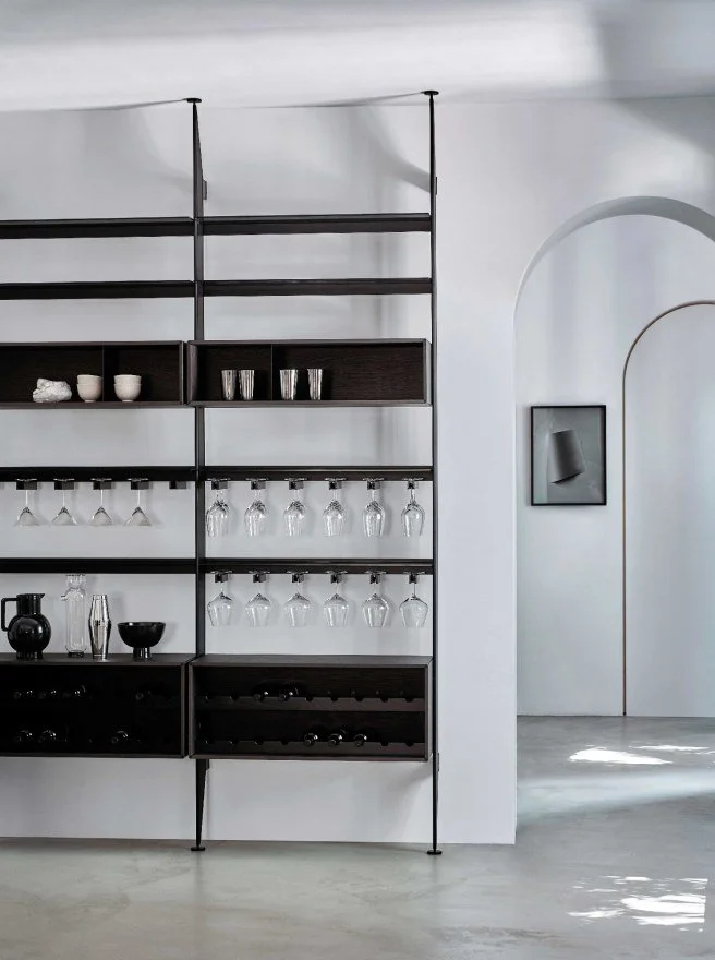Modern black metal and wood bar shelf with wine glasses, cups, and decorative items in a minimalist room.