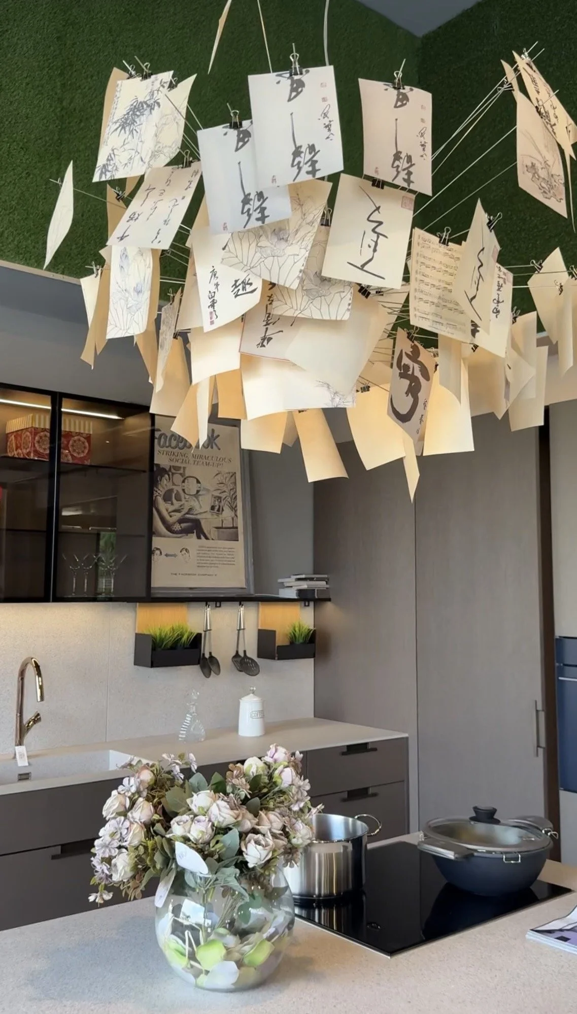 Kitchen with hanging artwork on the ceiling, a vase of flowers on the counter, and cooking pots on a stove.