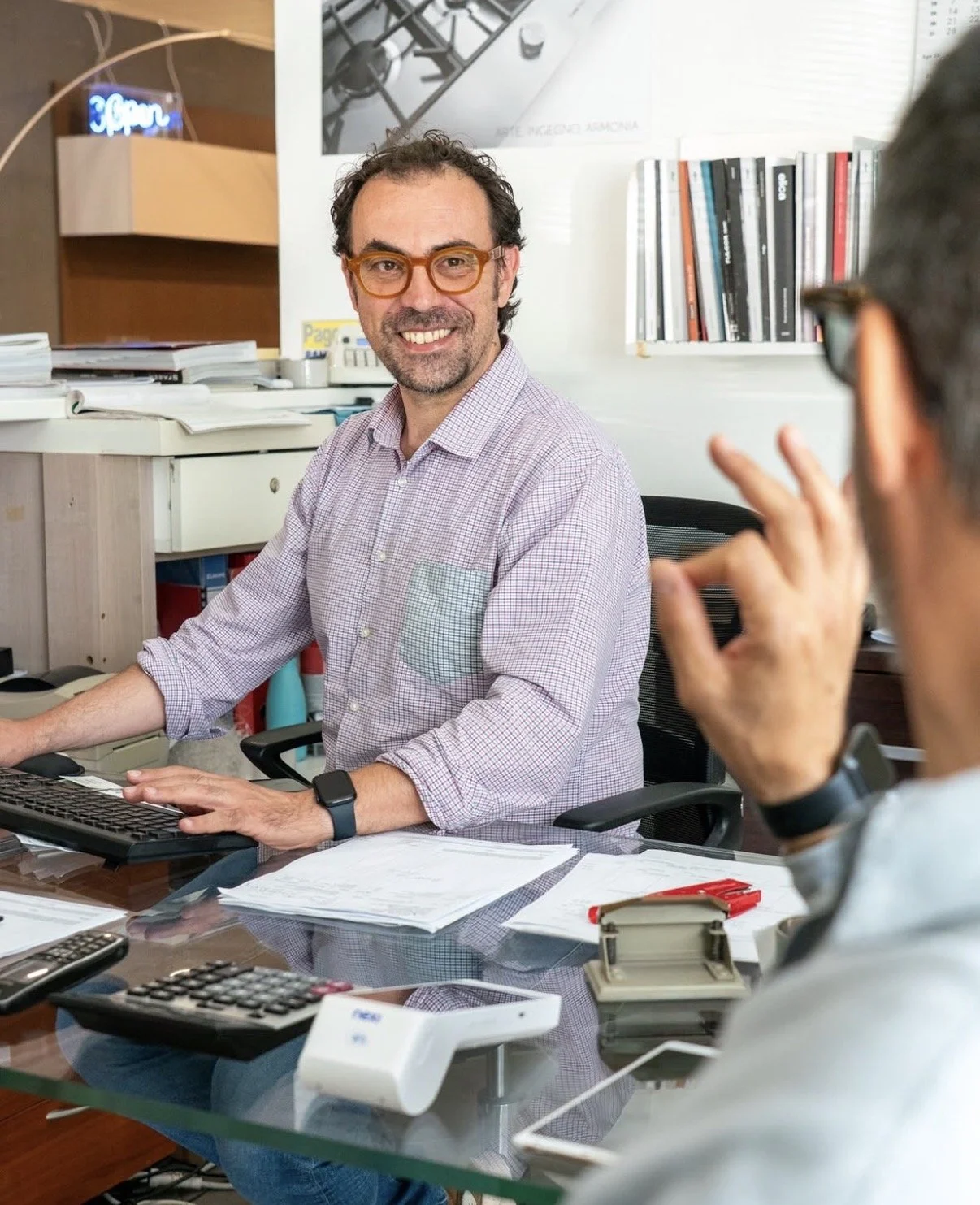 Two men having a conversation in an office, with one smiling at the camera and the other gesturing with his hand.