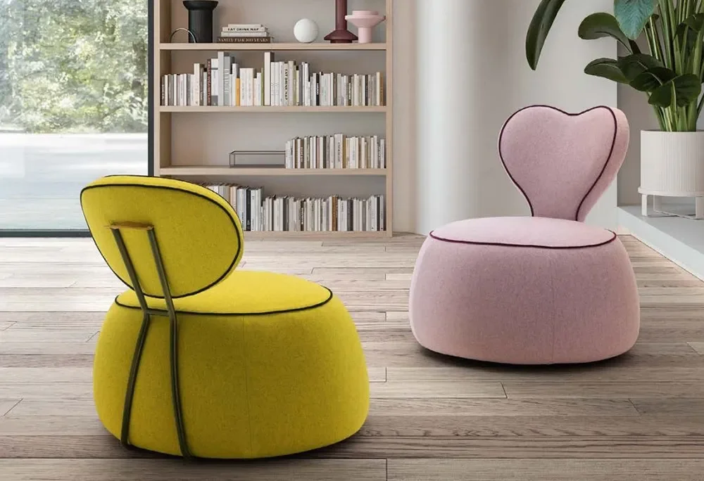 Yellow and pink modern lounge chairs in a cozy room with wooden flooring, a bookshelf, a large window, and a potted plant.