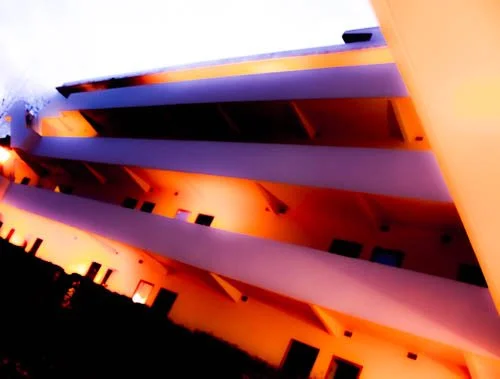 Low-angle view of a modern building at sunset with orange lighting, showcasing multiple ledges and windows.