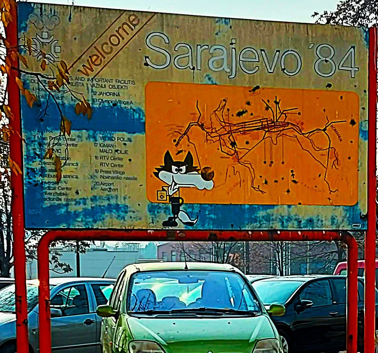 A welcome sign for Sarajevo 84, featuring a cartoon wolf with a camera, a map of the city, and informational text.