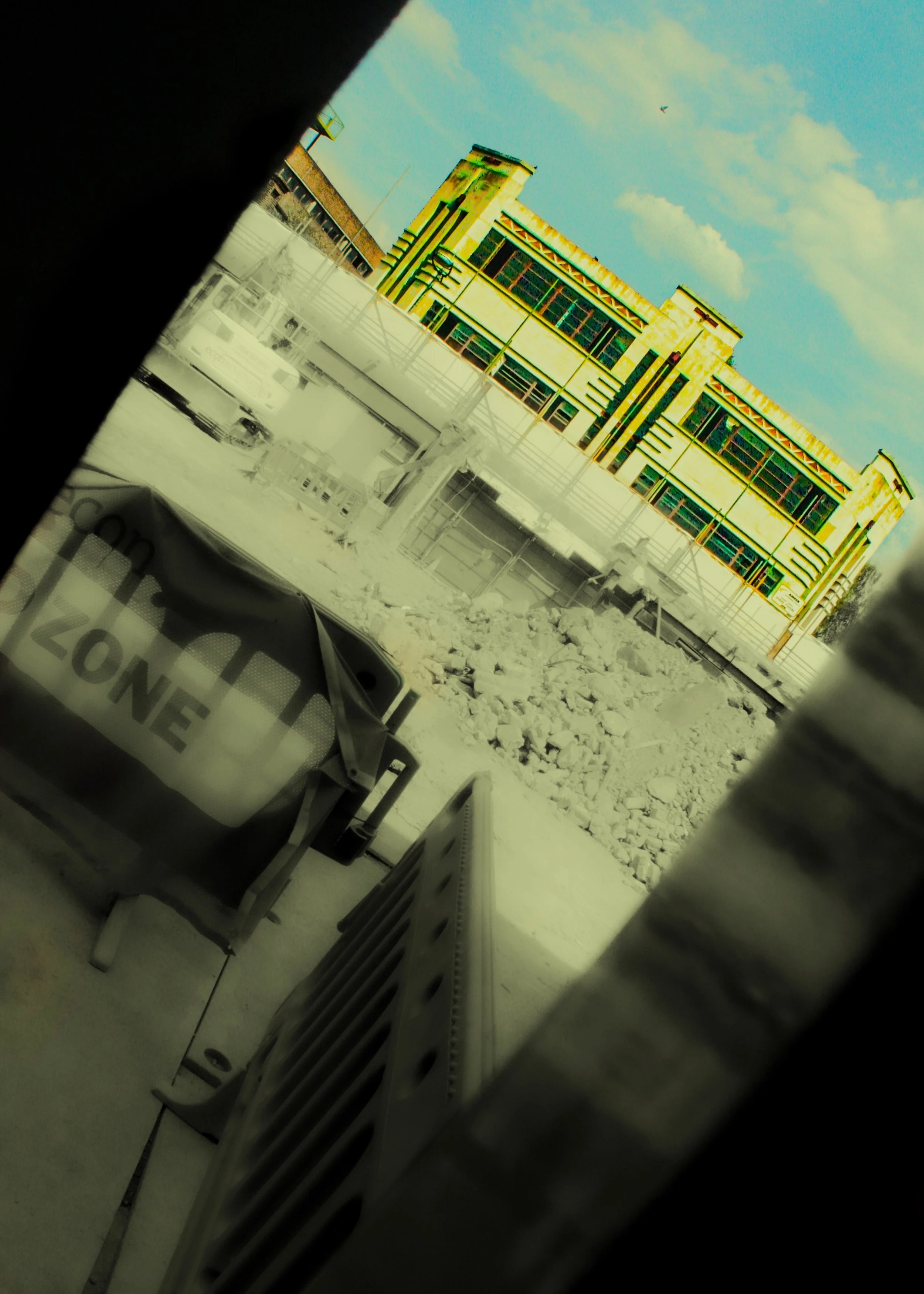 View of an art deco building with green and yellow accents, blue sky with clouds, and a bird flying. Snow and ice on the ground, benches and a partially visible sign that says "ONE" in the foreground.