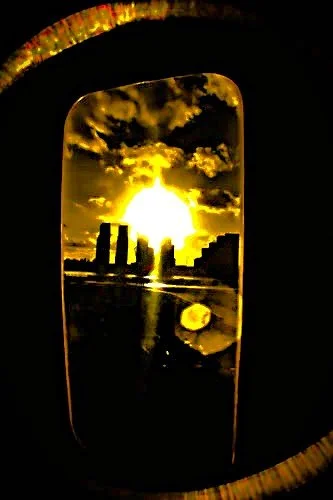 View of sunset through a window, with city skyline and clouds in the background.