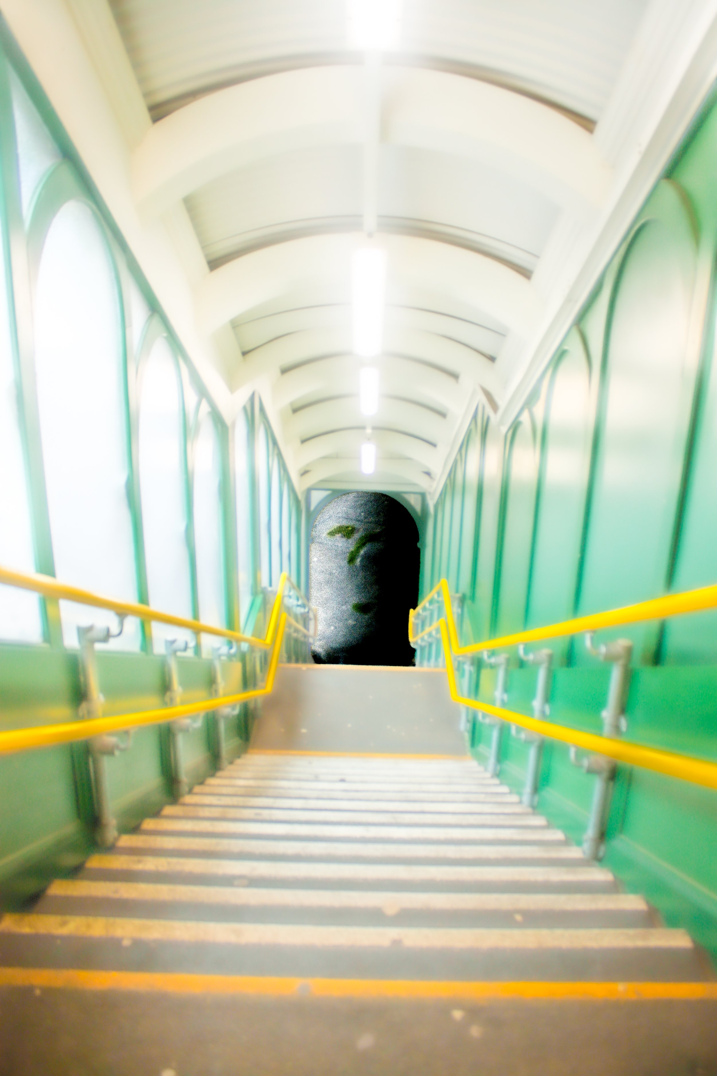 A staircase leading down, with green railings and a white arched ceiling, illuminated by overhead lights.