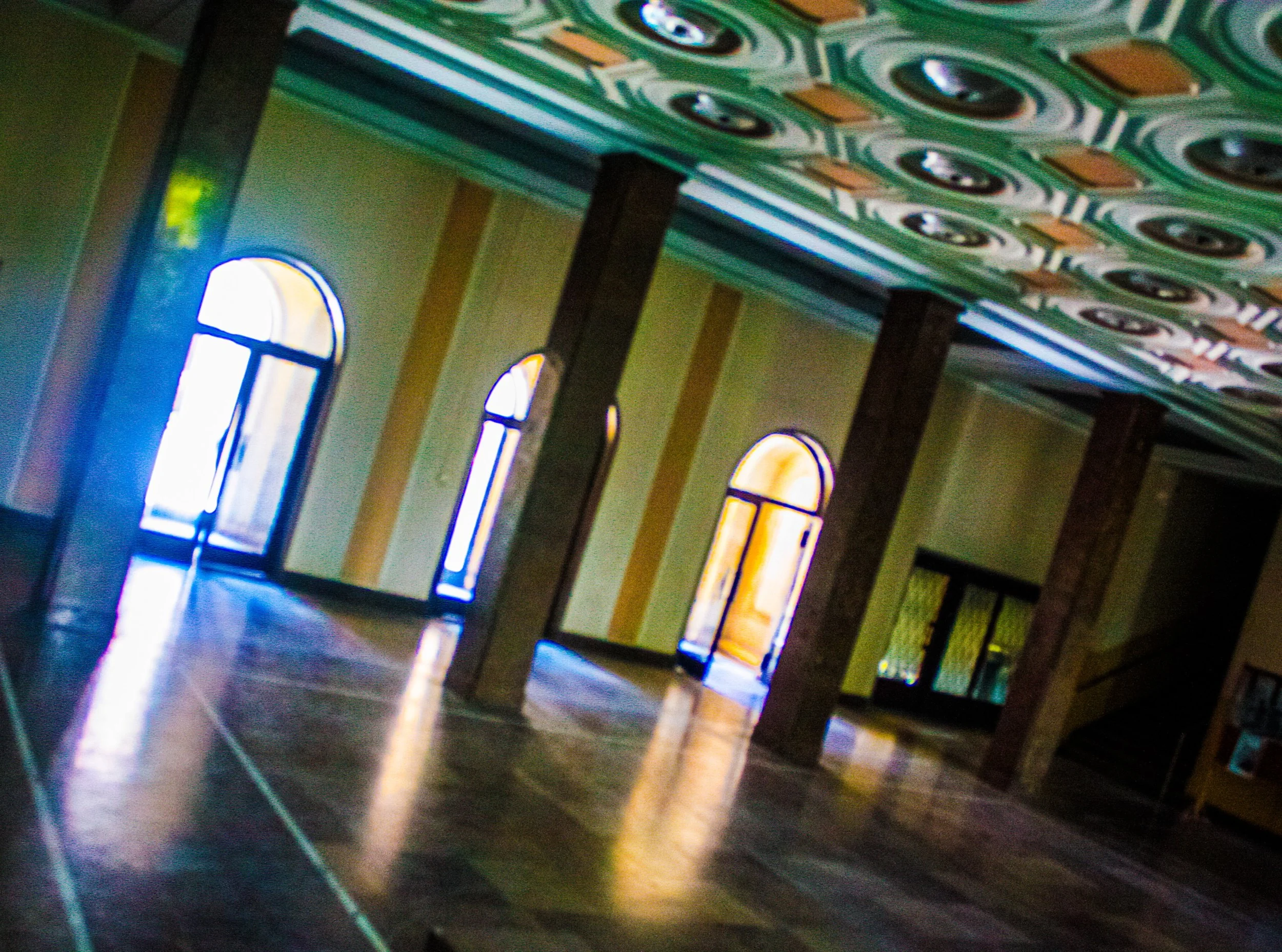 Interior of a room with large arched windows, wooden flooring, and patterned ceiling with circular designs.