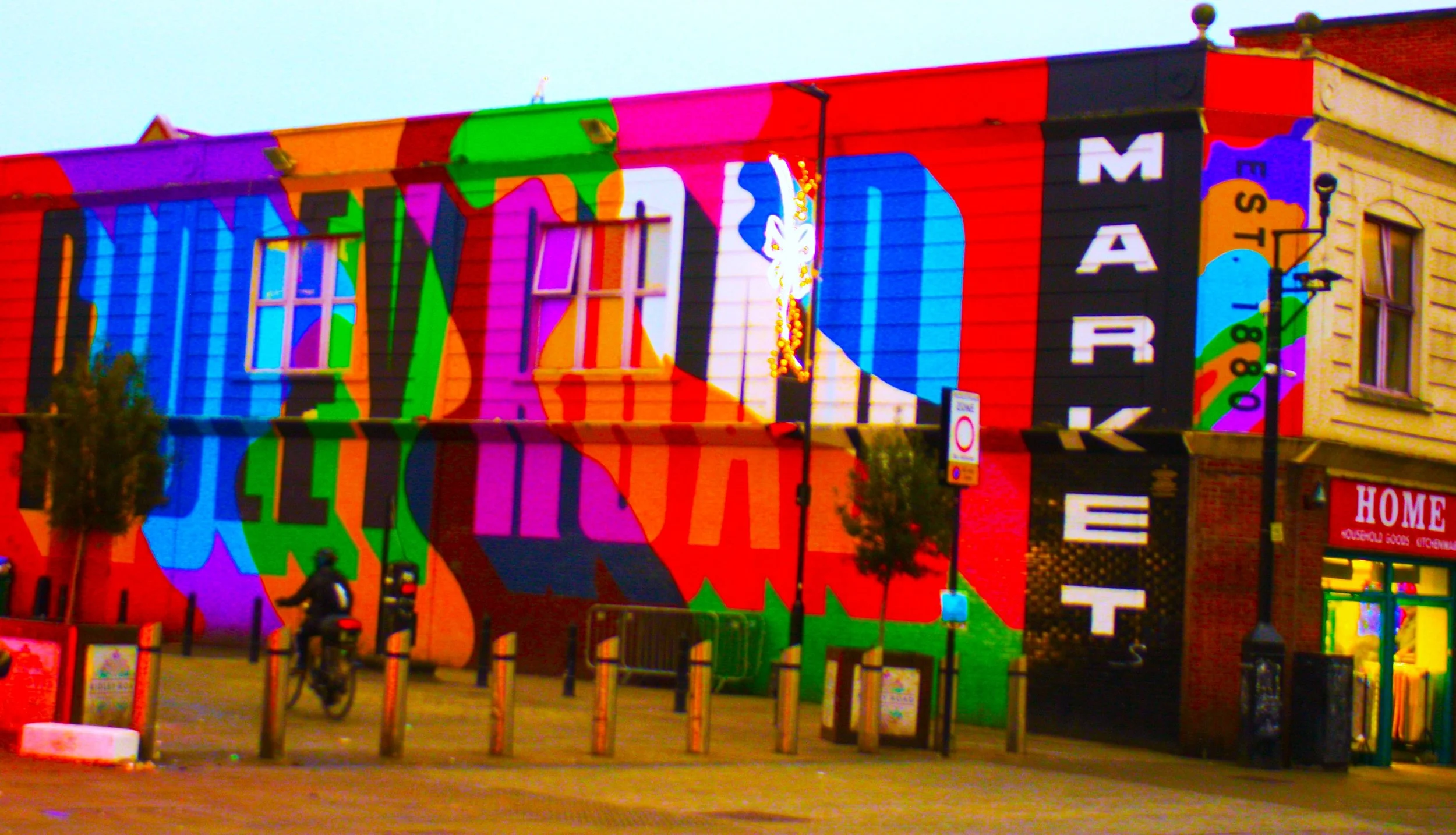 Colorful mural painted on the side of a building, featuring large, vibrant, overlapping letters and shapes in various bright colors.