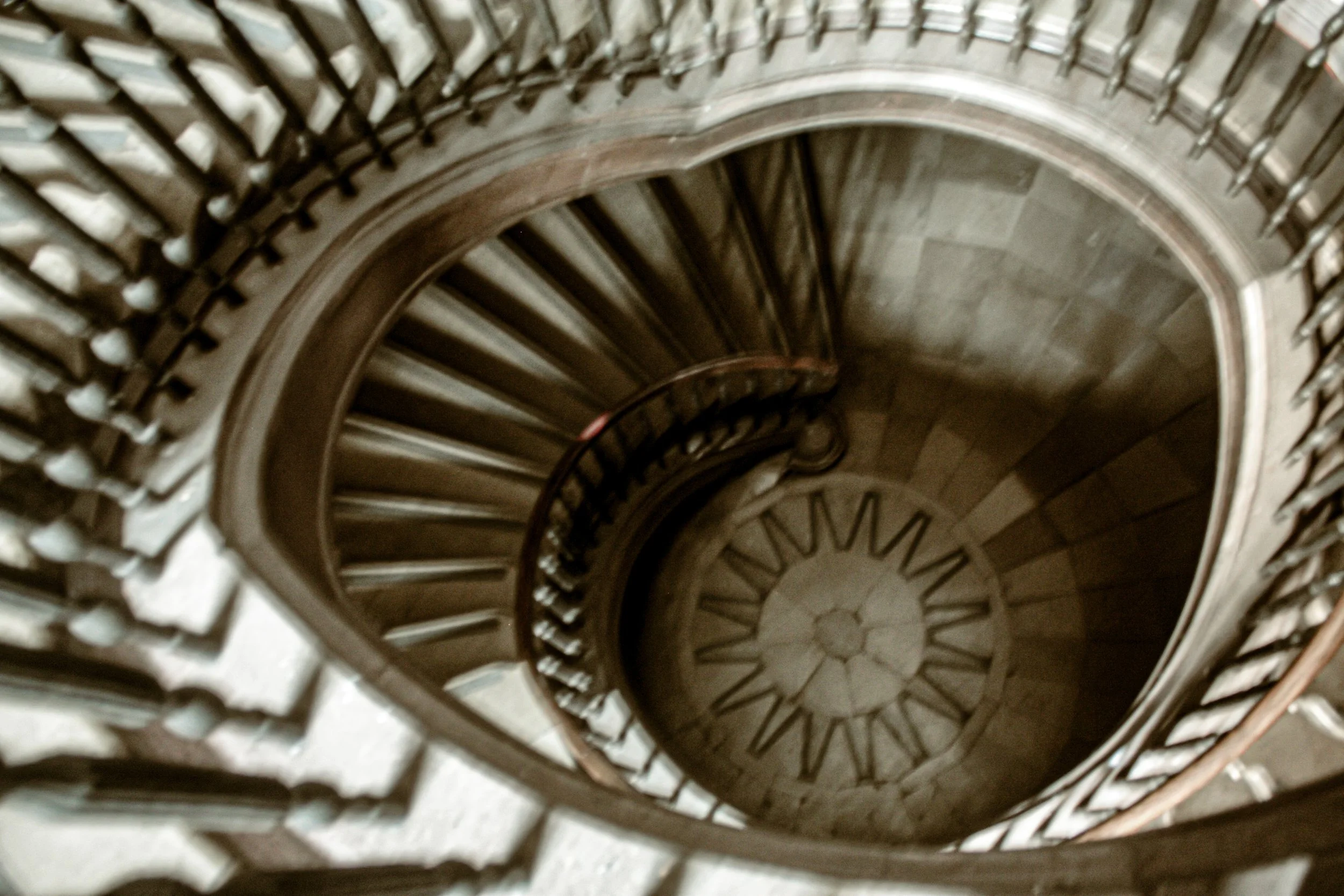 A spiral staircase seen from above, with wooden steps and decorative metal railings.