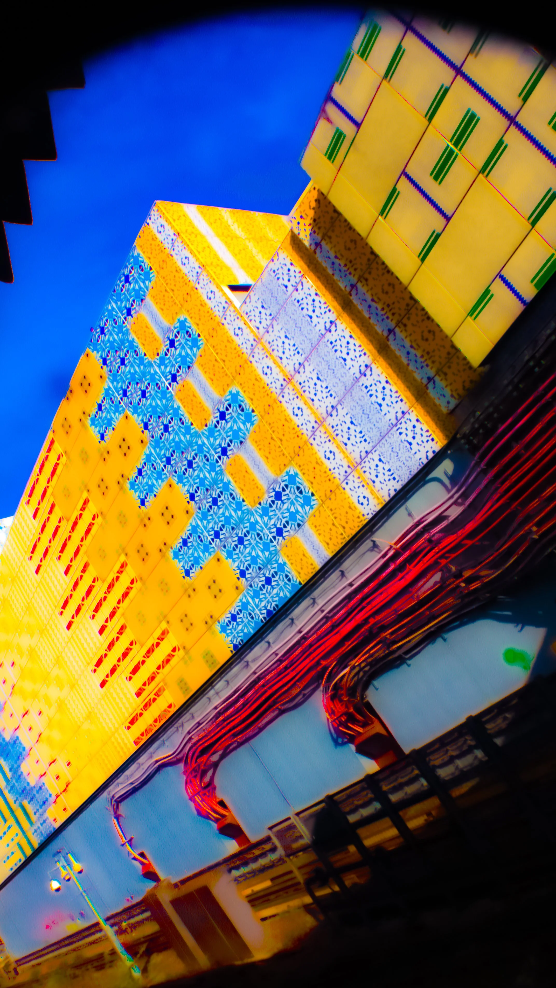 Close-up of a vibrant building with colorful, patterned exterior walls, set against a clear blue sky, with some visible urban infrastructure in the foreground.