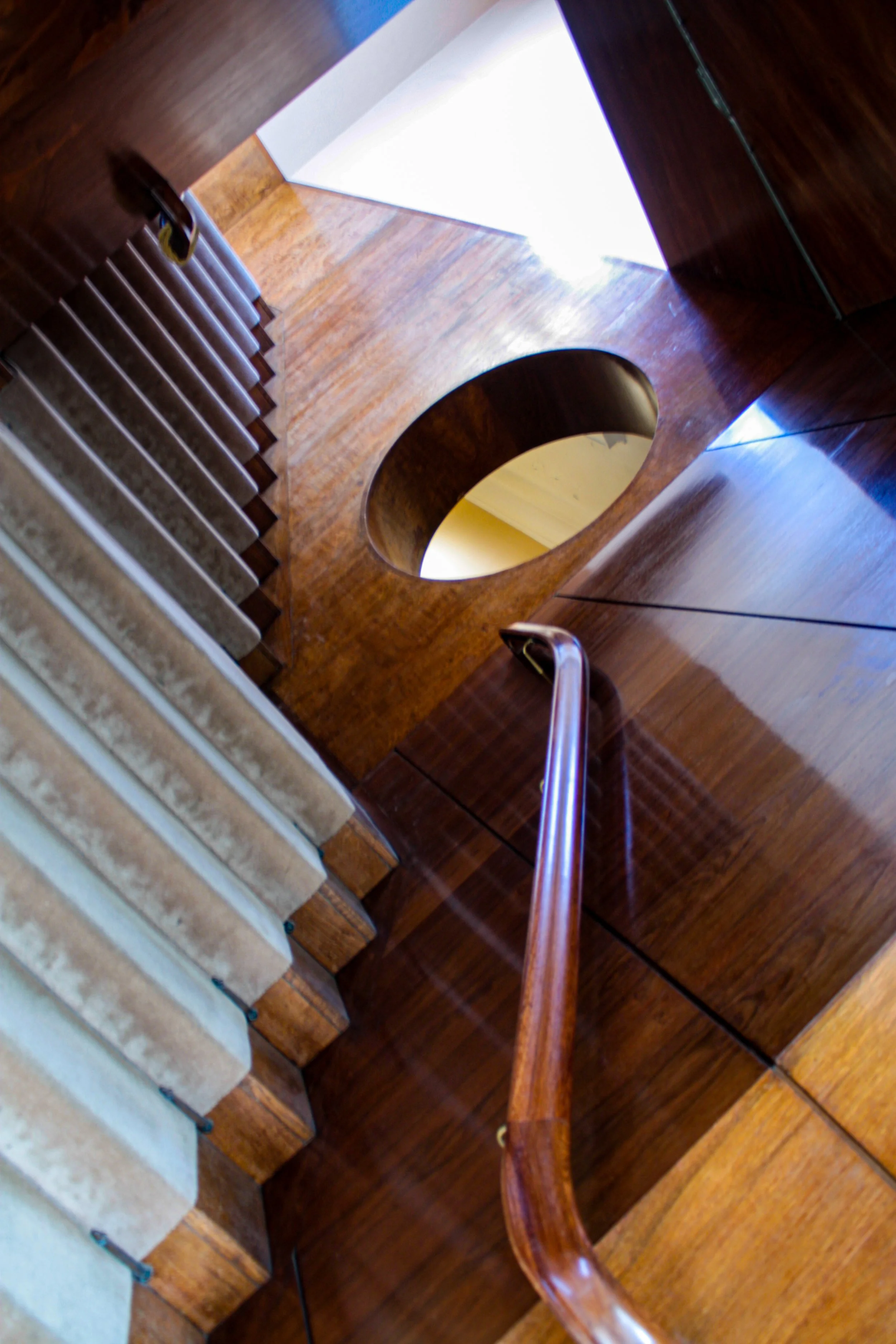 Photo taken from the top of a curved wooden staircase looking down and showing part of the staircase, wooden walls, and a bright window or light source at the top opening.