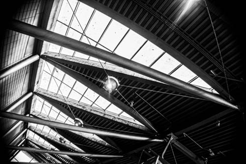 Interior view of a modern building with large glass ceiling and exposed beams, featuring spherical hanging light fixtures.