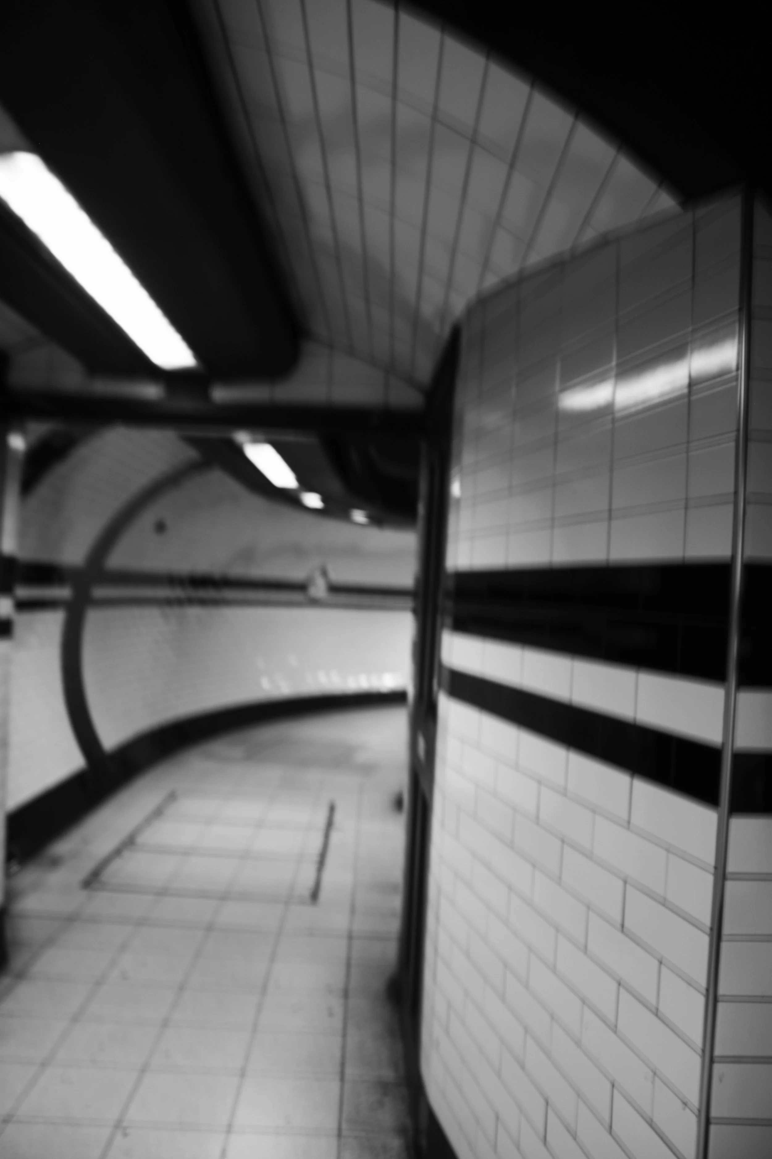 Underground subway station with tiled walls and curved ceiling, benches, and fluorescent lighting.