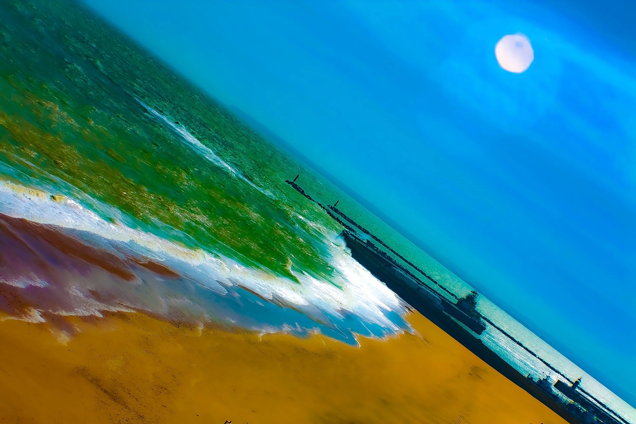 A scenic view of a beach with waves crashing onto the shore, a pier in the distance, and a bright full moon in a blue sky.