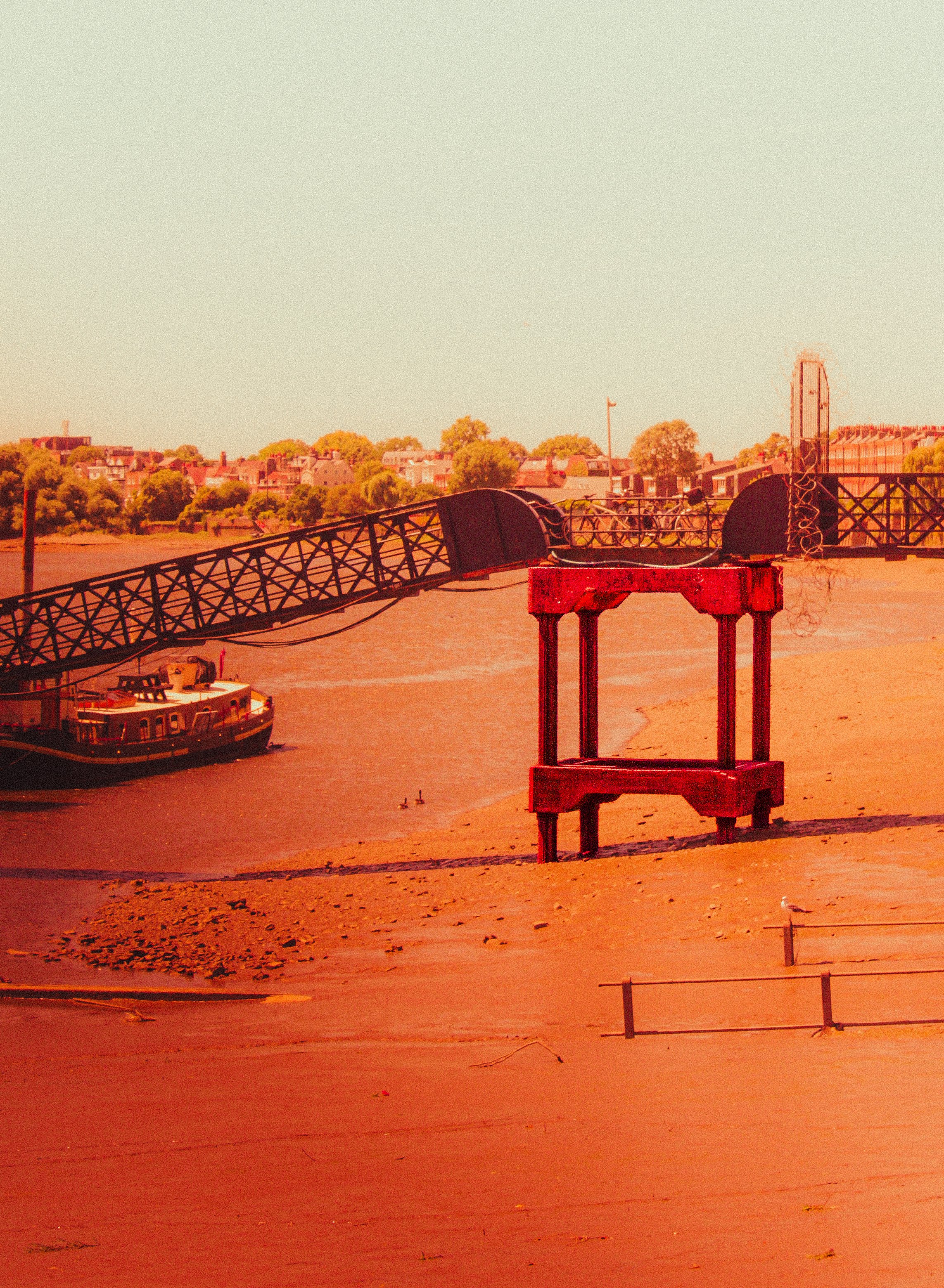 Sunset over a river with boats, a bridge, and a town in the background, with a wooden dock in the foreground.