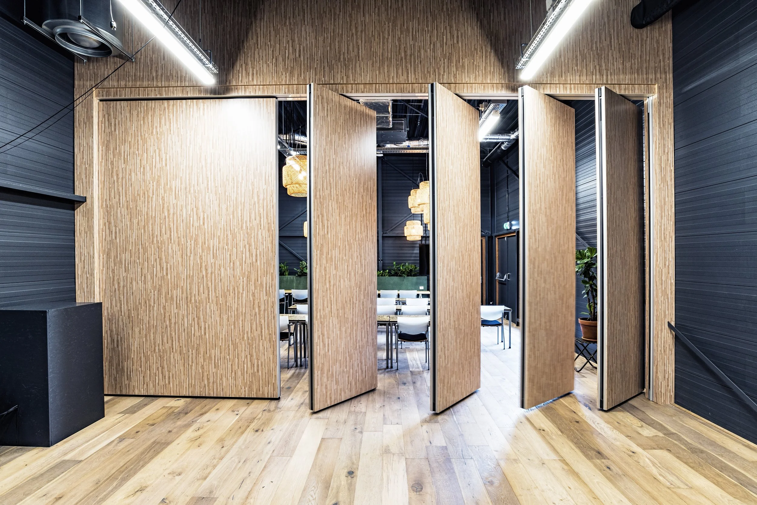 Modern interior with wooden wall dividers, black walls, hanging pendant lights, and seating area with chairs and a table.