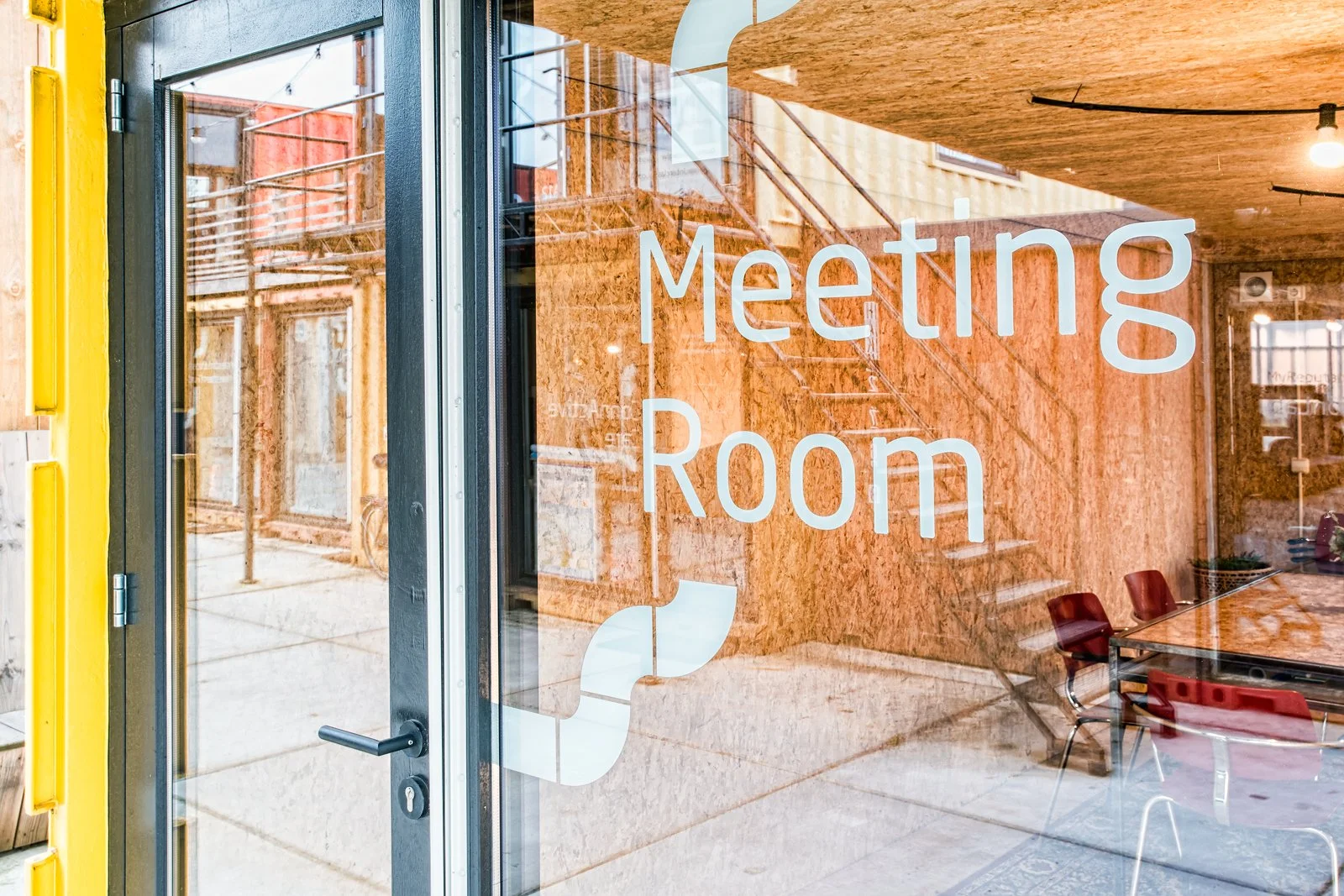 Glass door with white text reading 'Meeting Room' and a classroom with chairs visible inside.